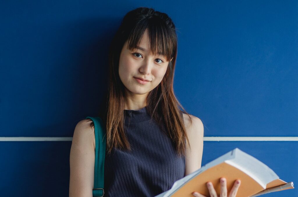 charming asian student with exercise books near blue wall